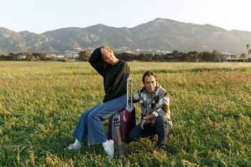 Fototapeta na wymiar Picture of female and male holding hands, sitting on suitcase on the field outdoors