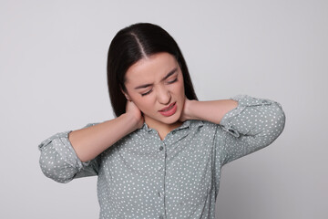 Young woman suffering from pain in neck on light grey background. Arthritis symptoms