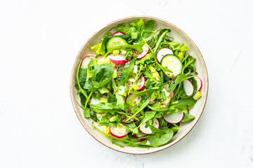 Green salad with spinach, arugula and radish with olive oil on white table.