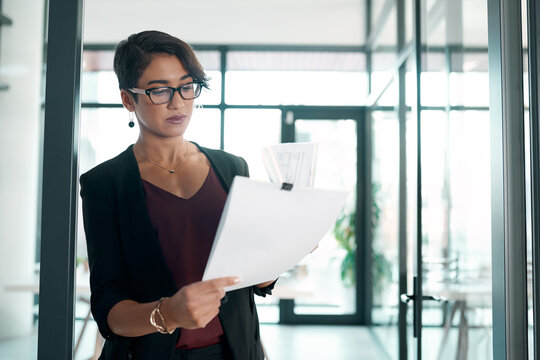 Hmm, theres definitely room for improvement. an attractive young businesswoman standing alone in the office and reading paperwork.