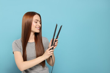 Fototapeta premium Beautiful woman with hair iron on light blue background, space for text