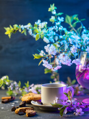 Obraz na płótnie Canvas white cup of tea or coffee on the table, white cherry blossom branches. Spring mood. colored light blue background