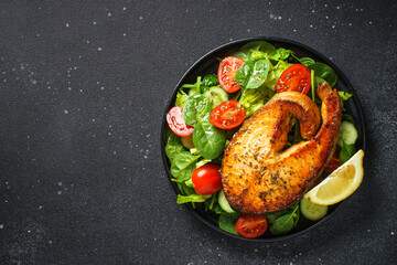 Salmon fish and green salad on black background. Baked salmon steak, Keto diet, healthy food. Top view with copy space.