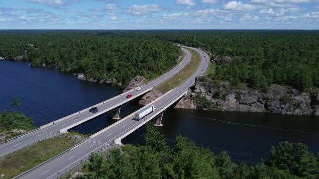 Rising aerial shot of curved highway bridge over lake through rock and trees near Gravenhurst Ontario