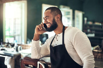 Ill see you in my salon soon. a handsome young barber standing alone in his salon and using his cellphone.