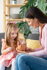 Mother holding a piggy bank and a cute little girl puts a coin in it. Children saving concept.