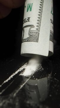 Vertical video. Simulating cocaine use, I pick up a rolled up dollar bill and suck up the powder on the black table. Dolly slider extreme close-up.