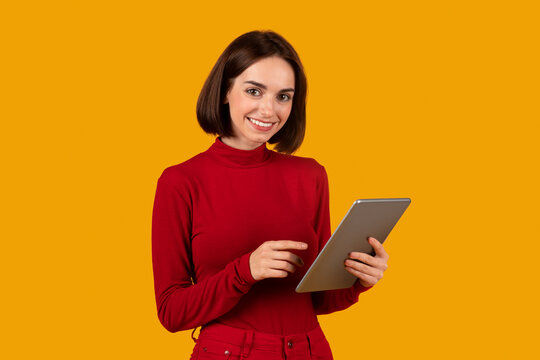 Cheerful pretty young woman digital nomad using tablet on orange Generative AI