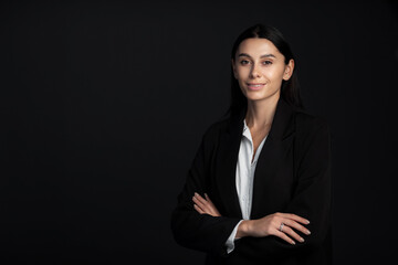 Portrait of smiling business woman with cross hands in formal suit on black background. Beautiful...