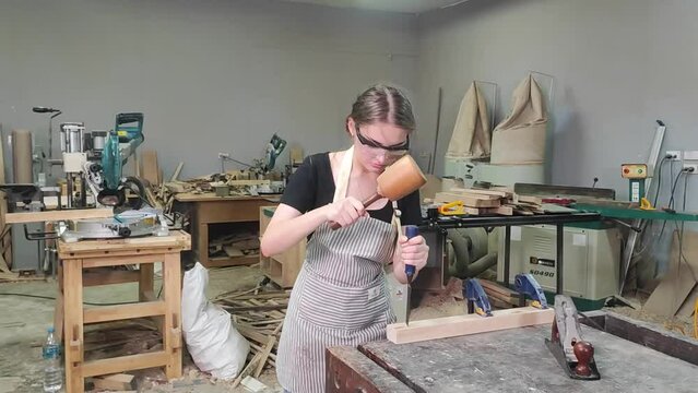 Woodworking Artisan: A young woman, focused and diligent, works with chisel and mallet on a piece of wood in her workshop, surrounded by tools and materials, embodying craftsmanship and dedication.