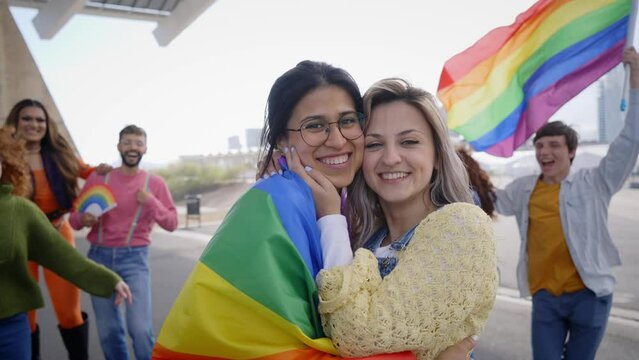 Lesbian couple with a Group of excited young friends enjoying together on gay pride day. Joyful people gathered from LGBT community hugging laughing outdoors. Generation z and open mind