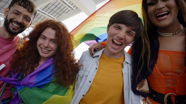 Group of excited young friends enjoying together on gay pride day. Joyful people gathered from LGBT community hugging laughing outdoors. Generation z and open minded. 