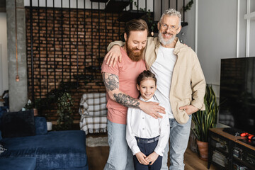 Smiling homosexual couple hugging preteen daughter at home. 
