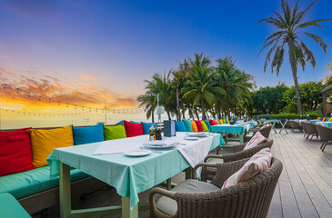 Seaside restaurant,Beach club concept, food corner or cafe, restaurant tables, straw natural chairs, wooden tables, makrome knitted sun umbrellas, white modern sun beds, sea view on background