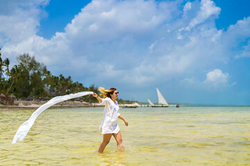 Beach holiday - beautiful woman holding shawl walking on sunny, tropical beach