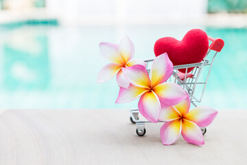 Beautiful plumeria flower with red heart in shopping cart over blurred background, tropical summer, love and romance