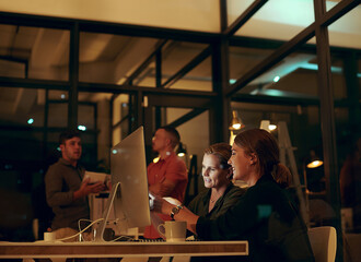 With a few extra hours, well get so much done. two businesswoman looking at something on a computer in an office at night.