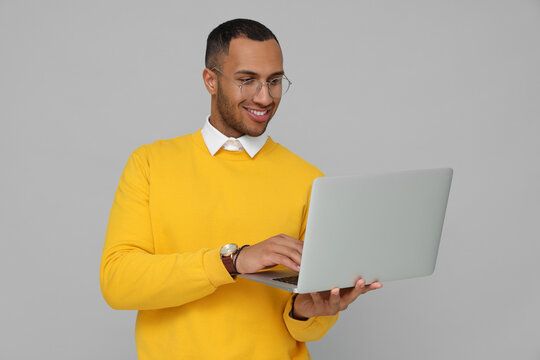 Happy young intern working on laptop against light grey background