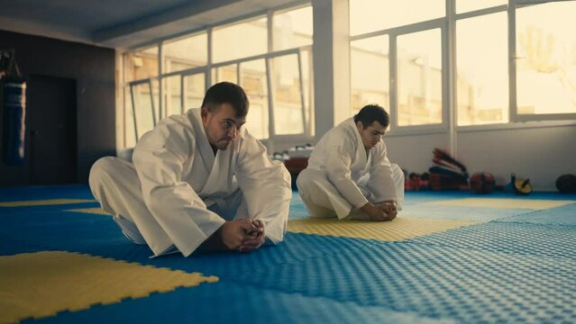 Men in white kimonos stretching before taekwondo sparring, training partners