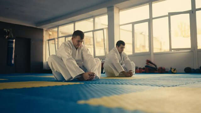 Two young men exercising before practicing martial art, master and student