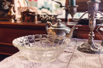 Vintage furniture and glassware on table with napkin. Silver teapot and candlestick. Retro interior of coffee shop