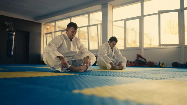Men in white uniform preparing for class in martial art school, warming up