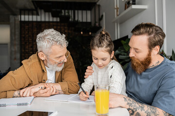 Preteen girl doing homework with same sex parents near notebooks and digital tablet at home. 
