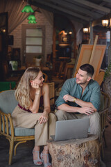 Vertical portrait. A young couple with a relaxed lifestyle. Young couple sitting and talking and making plans working on a laptop computer in her studio