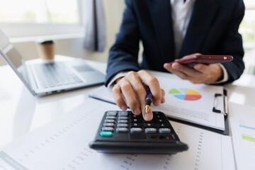 Asian businessman working at office with laptop, tablet and graph data sheet on his desk.