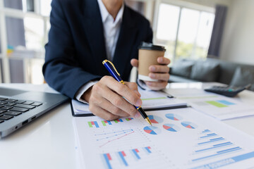 A business man working on a laptop comparing details from graphs Business income chart in real estate, tax, management, marketing, technology in private office.