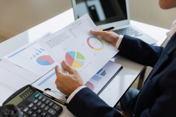 A business man working on a laptop comparing details from graphs Business income chart in real estate, tax, management, marketing, technology in private office.