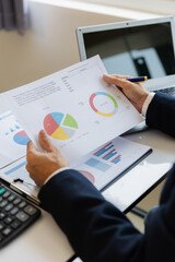 A business man working on a laptop comparing details from graphs Business income chart in real estate, tax, management, marketing, technology in private office.