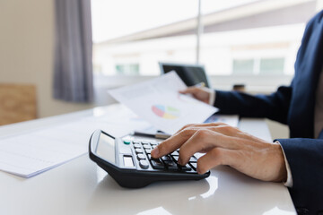 A business man working on a laptop comparing details from graphs Business income chart in real estate, tax, management, marketing, technology in private office.