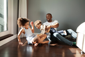 Happy Young Black Family Playing Together On Floor At Home In Living Room. Funny dad having fun with two kids. African american father with children, real people emotion