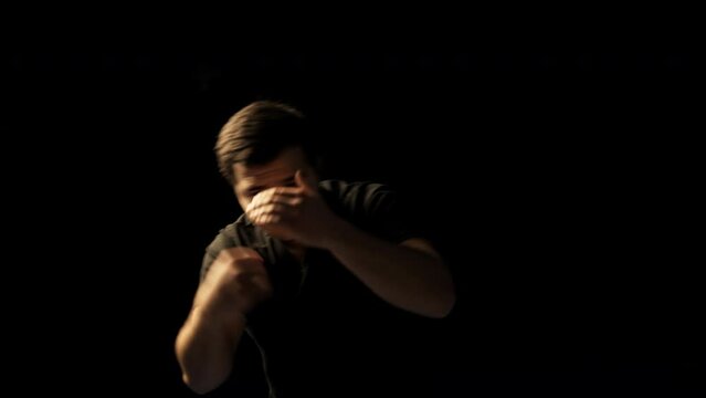 Young athletic man shadowboxing on black background, solo training practice