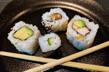 Sushi mit Stäbchen auf schwarzem Teller