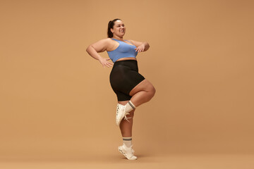 Young, positive woman with overweight figure training in sportswear against brown studio background. Cardio exercises. Concept of sport, body-positivity, weight loss, body and health care. Ad
