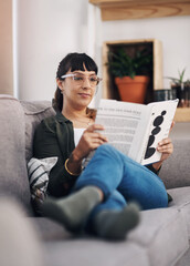 Obraz premium I am totally intrigued with this book. Full length shot of an attractive young woman sitting alone in her living room and reading a book.