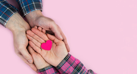 Woman's and man's hands hold a pink heart on a pink background. The concept of love, family and friendship. Banner. Top view. Place for text. Selective focus.