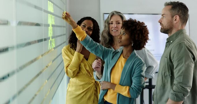 Diverse group of businesspeople laughing while having an office brainstorming session using adhesive notes on a glass wall