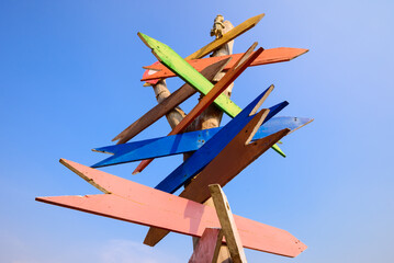 Colorful wooden signpost, multiple direction arrows on tree trunk isolated on blue sky