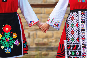 Girls in traditional bulgarian ethnic costumes with folklore embroidery holding hands. The spirit...