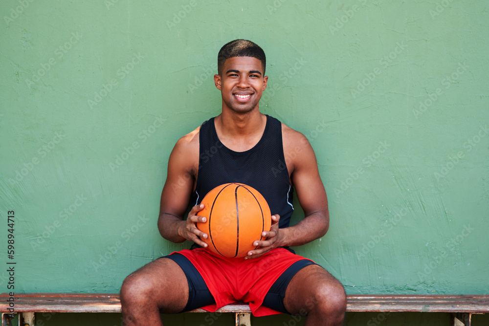 Poster Hes got that Shaq attack. Portrait of a sporty young man holding a basketball while sitting on a bench against a wall.