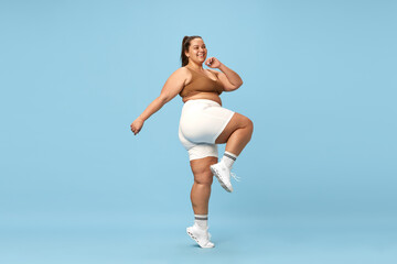 Fototapeta na wymiar Young, positive, smiling overweight woman training in sportswear, running, doing cardio exercises against blue studio background. Concept of sport, body-positivity, weight loss, body and health care