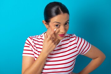 beautiful woman wearing striped T-shirt over blue studio background , looking, observing, keeping an eye on an object in front, or watching out for something.