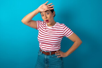 beautiful woman wearing striped T-shirt over blue studio background wiping forehead with hand...