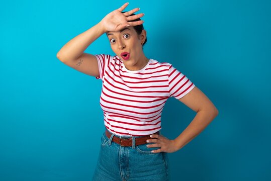 beautiful woman wearing striped T-shirt over blue studio background wiping forehead with hand making phew gesture, expressing relief feels happy that he prevented huge disaster. It was close enough