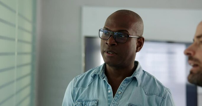 Two diverse businessmen talking and smiling while having a casual meeting together in the boardroom of an office