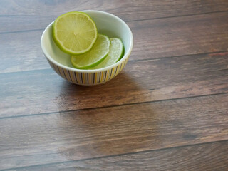Slices of lime fruit in a bowl on a wooden table 