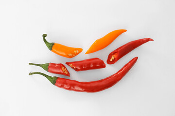 Whole and cut different hot chili peppers on white background, flat lay